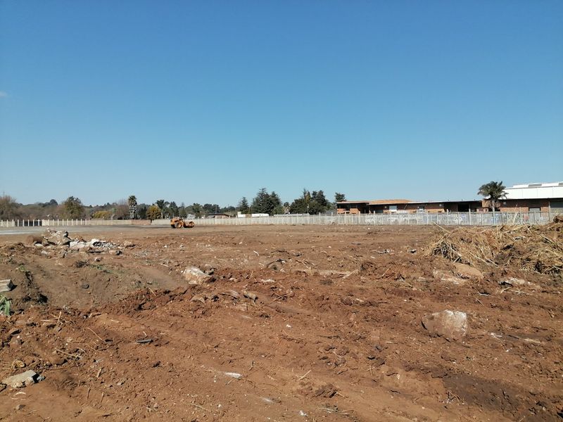 A wide-angle view of a vacant residential plot featuring cleared earth, uneven terrain, and perimeter fencing in a suburban setting.