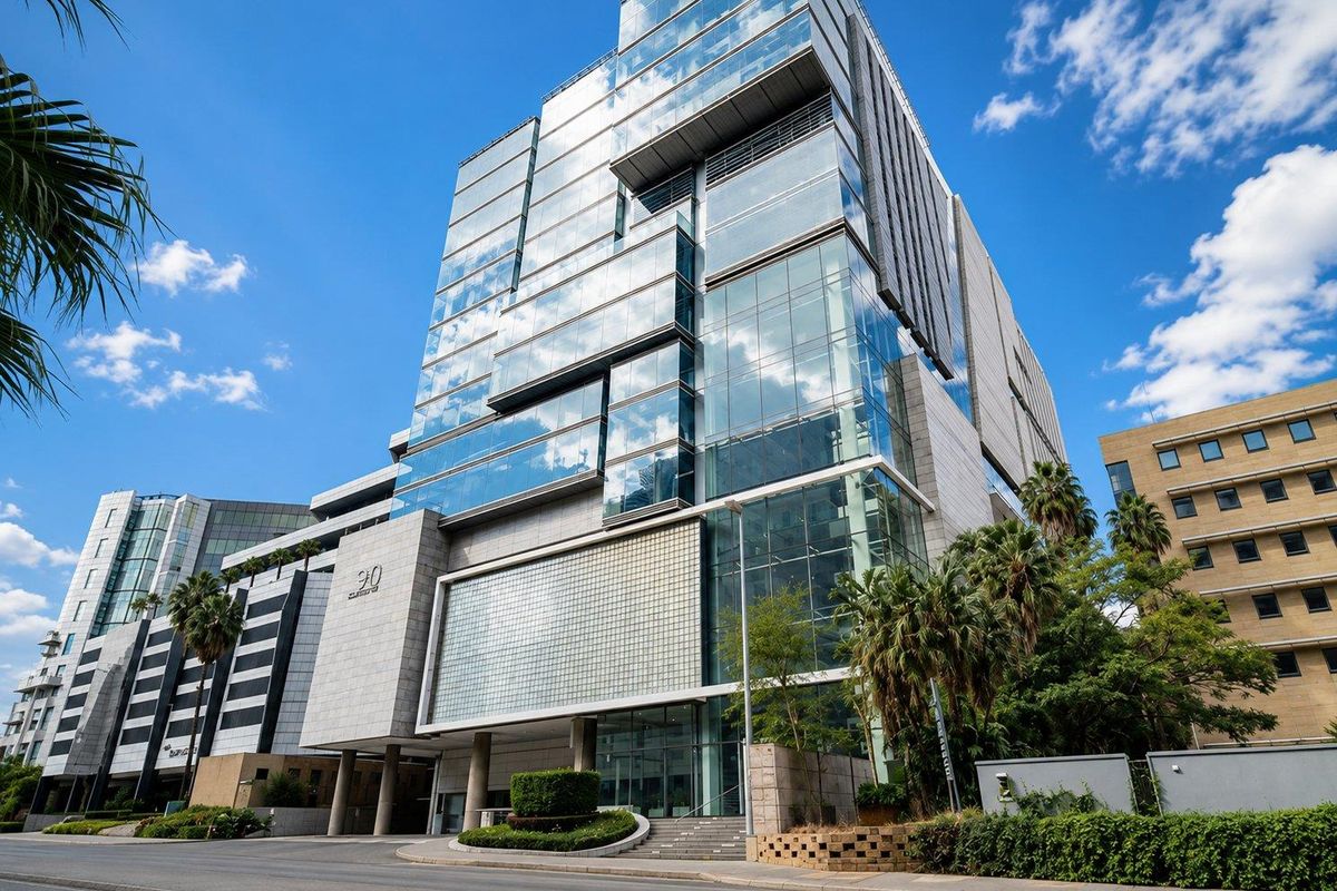 Modern commercial office building featuring a prominent glass curtain wall facade, stone cladding, and professional landscaping at the street-level entrance.