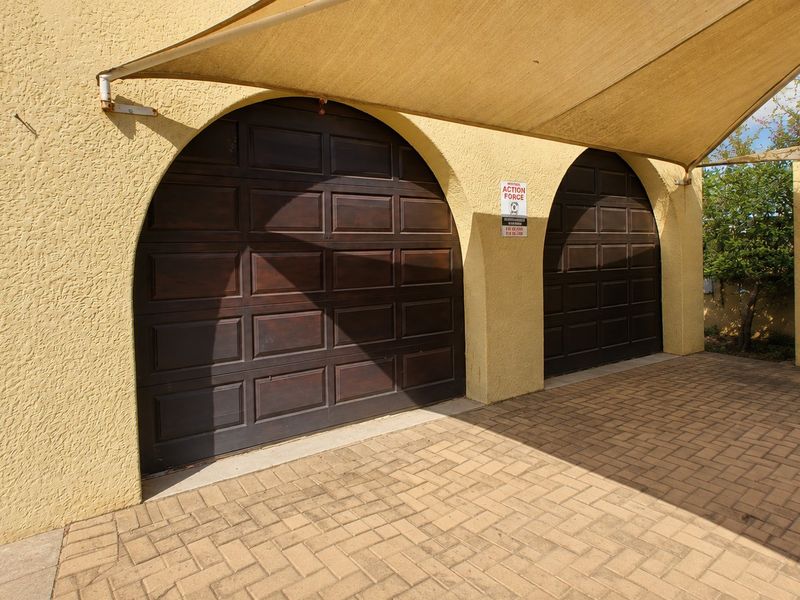 A double garage featuring arched wooden doors and a paved driveway area covered by a shade sail.
