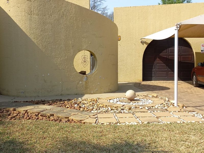 Front exterior view featuring a unique curved architectural facade, paved driveway, double garage with shade sail, and landscaped stone garden area.