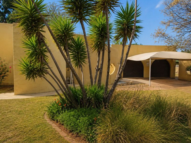 Front exterior view of a house featuring a stucco facade, double garage with a shade sail, and a landscaped garden area.