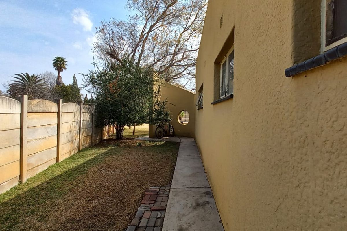A side view of the property showing a concrete pathway, a precast boundary wall, and a textured exterior wall with a circular feature window.