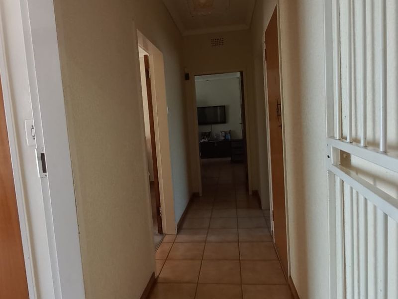 A functional hallway featuring tiled flooring, built-in storage cupboards, and a security gate, providing access to adjacent rooms within the home.