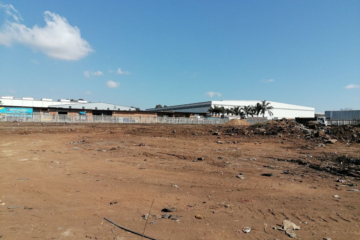 A vacant residential plot featuring cleared land and perimeter fencing, situated in an industrial-adjacent area.