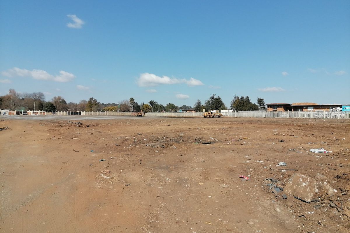 A wide-angle view of a vacant residential plot featuring cleared land, perimeter fencing, and surrounding neighborhood infrastructure.