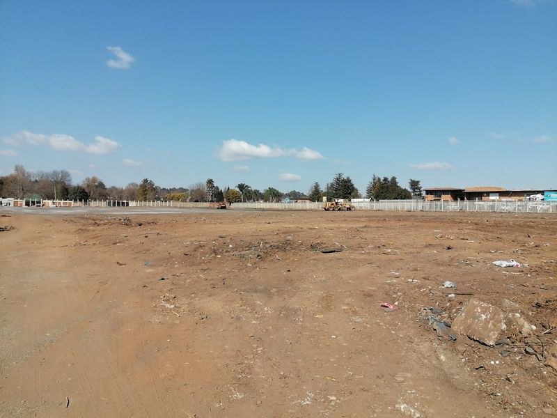 A wide-angle view of a vacant residential plot featuring cleared land, perimeter fencing, and surrounding neighborhood infrastructure.