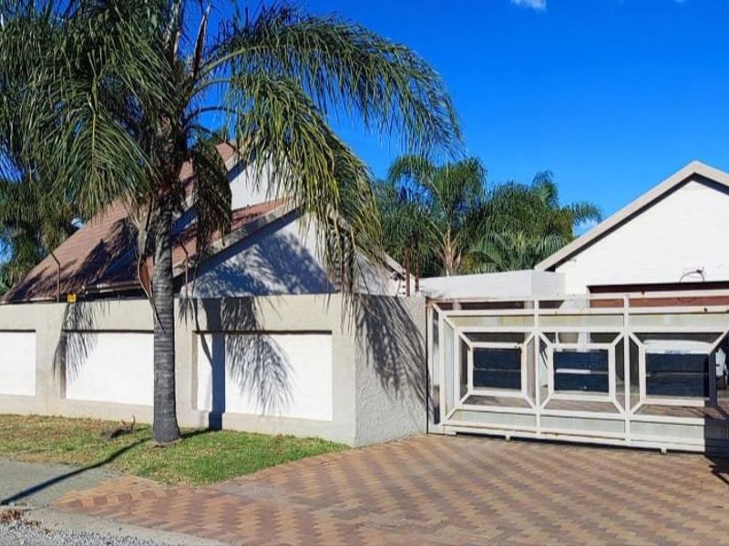 Front exterior view of the property featuring a secure perimeter wall with electric fencing, a sliding driveway gate, and a paved driveway.