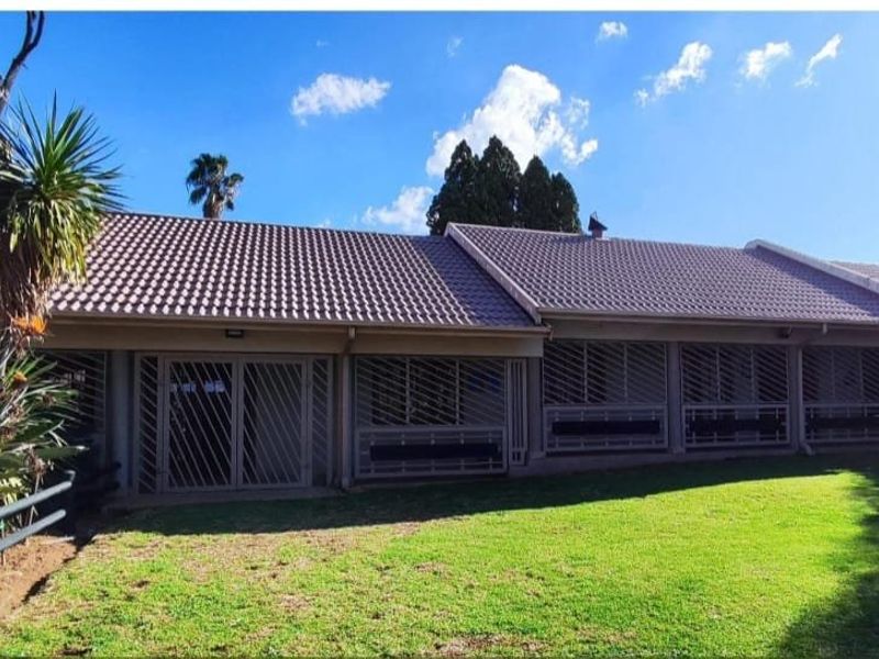 Rear view of the house featuring a tiled roof, security-gated patio area, and a well-maintained lawn.