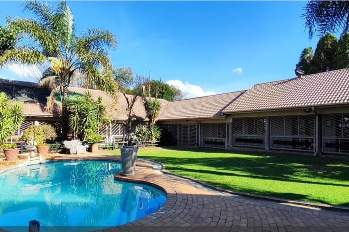Spacious rear exterior featuring a well-maintained swimming pool, brick paved surround, lush lawn, and secure building facade with fitted security shutters.