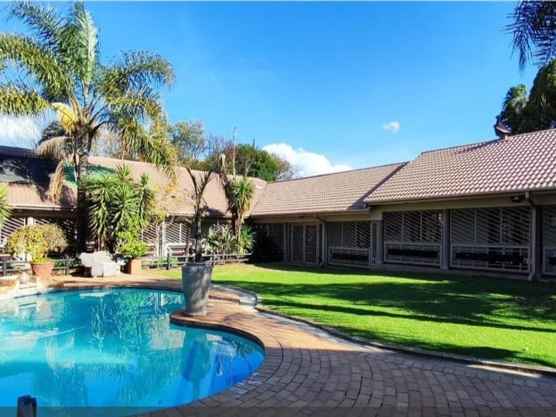Spacious rear exterior featuring a well-maintained swimming pool, brick paved surround, lush lawn, and secure building facade with fitted security shutters.