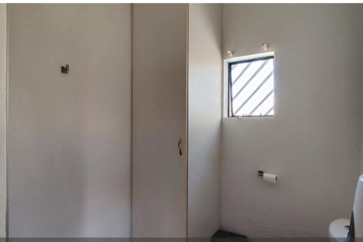 A basic bathroom featuring a toilet, a built-in storage cupboard, and a small window with security bars.