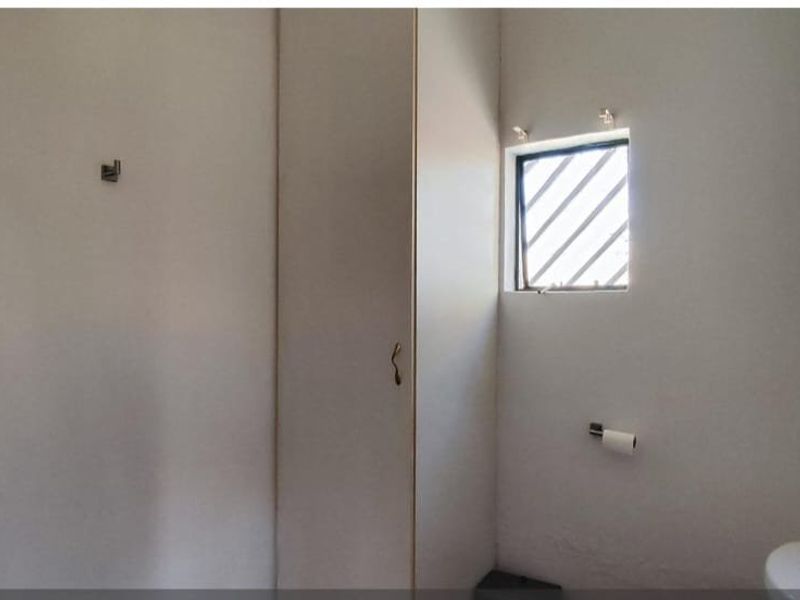 A basic bathroom featuring a toilet, a built-in storage cupboard, and a small window with security bars.