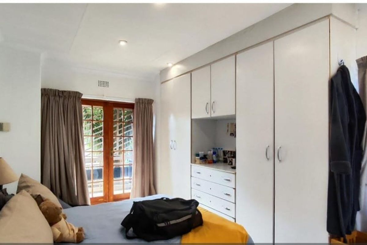 A bedroom featuring built-in cupboards, recessed downlights, and wooden french doors providing access to the exterior.