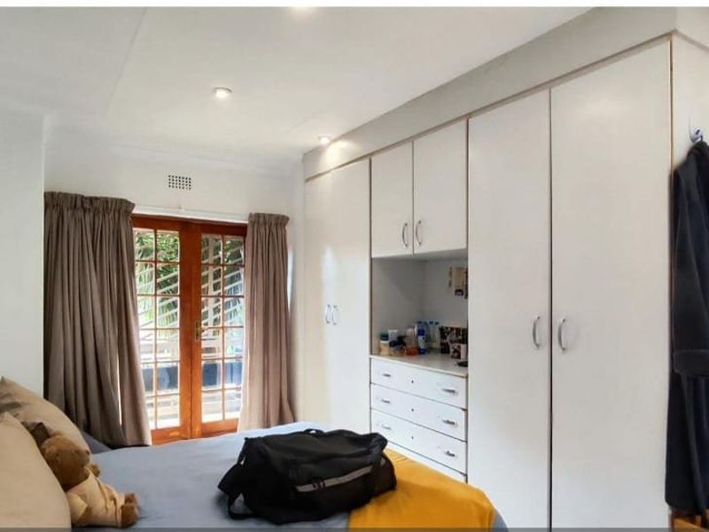 A bedroom featuring built-in cupboards, recessed downlights, and wooden french doors providing access to the exterior.