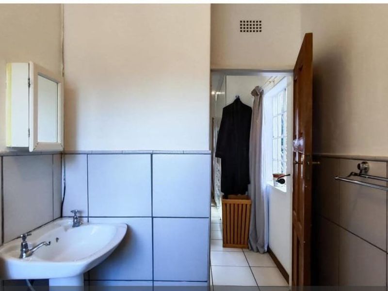 A functional bathroom featuring tiled walls, a pedestal basin, and a medicine cabinet, with a doorway leading to an adjacent space.