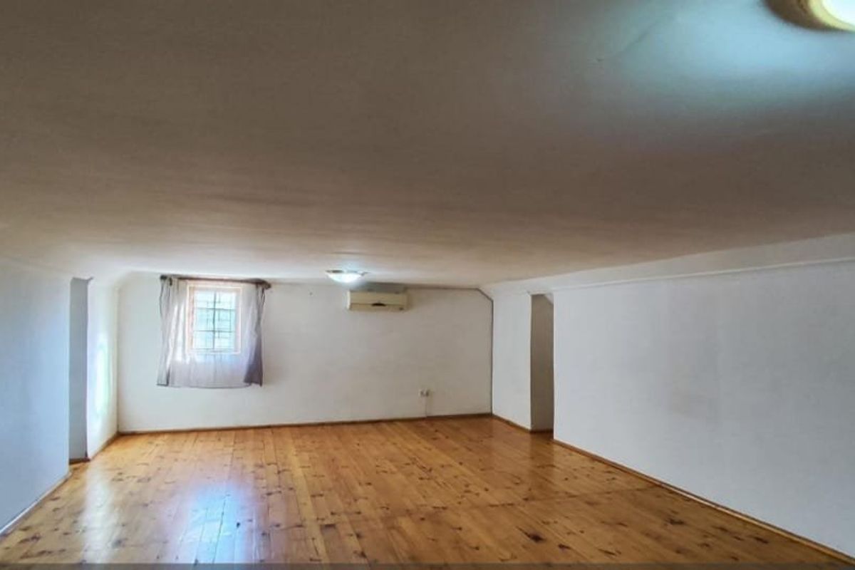 A spacious, empty living area featuring polished hardwood flooring, a wall-mounted air conditioning unit, and neutral white walls.