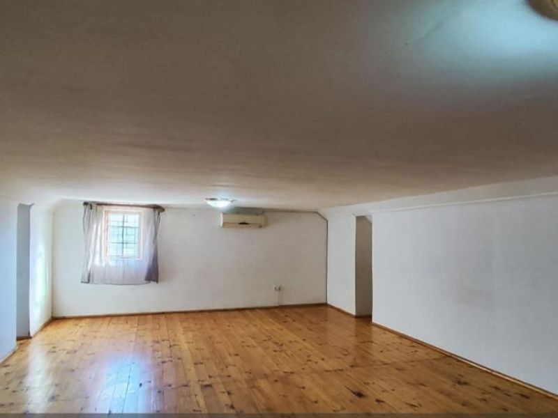 A spacious, empty living area featuring polished hardwood flooring, a wall-mounted air conditioning unit, and neutral white walls.