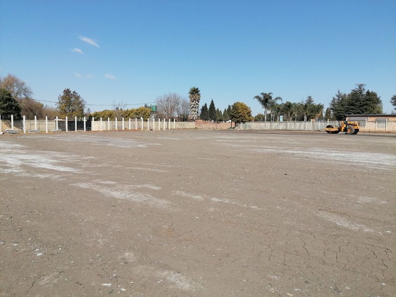 A large, cleared vacant residential plot enclosed by a concrete perimeter wall and security fencing, ready for development.