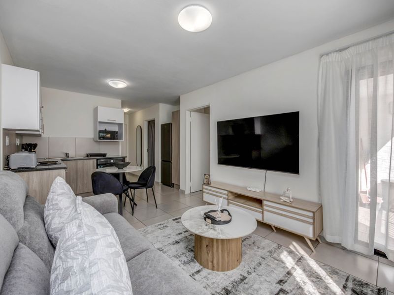 A modern open-plan living area featuring a compact kitchen with built-in cabinetry, tiled floors, and direct access to an outdoor space via a sliding door.