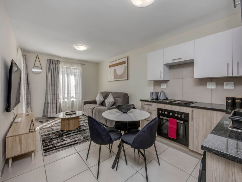 A well-maintained open-plan living and kitchen area featuring modern cabinetry, granite countertops, built-in appliances, and neutral tiled flooring throughout.