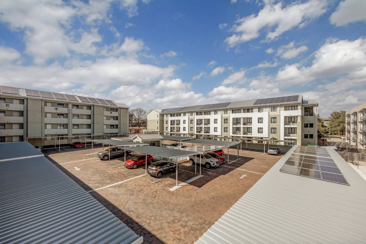 Aerial view of an apartment complex featuring paved parking with covered carports and solar panel installations on the building roofs.