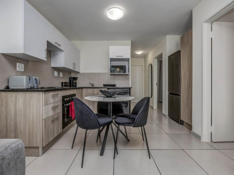 Modern kitchen featuring light wood-grain cabinetry, dark laminate countertops, built-in oven, hob, and tiled flooring in an open-plan layout.