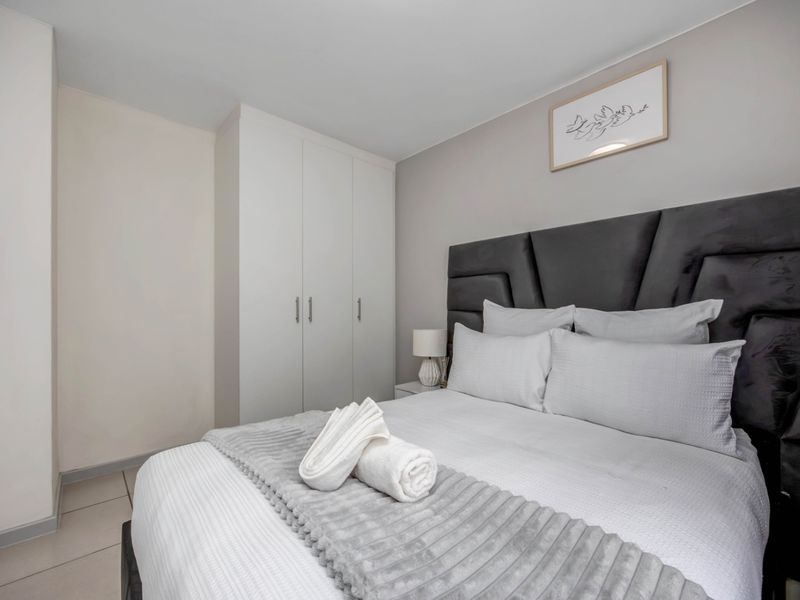 A well-maintained bedroom featuring neutral walls, tiled flooring, and a functional built-in wardrobe for storage.