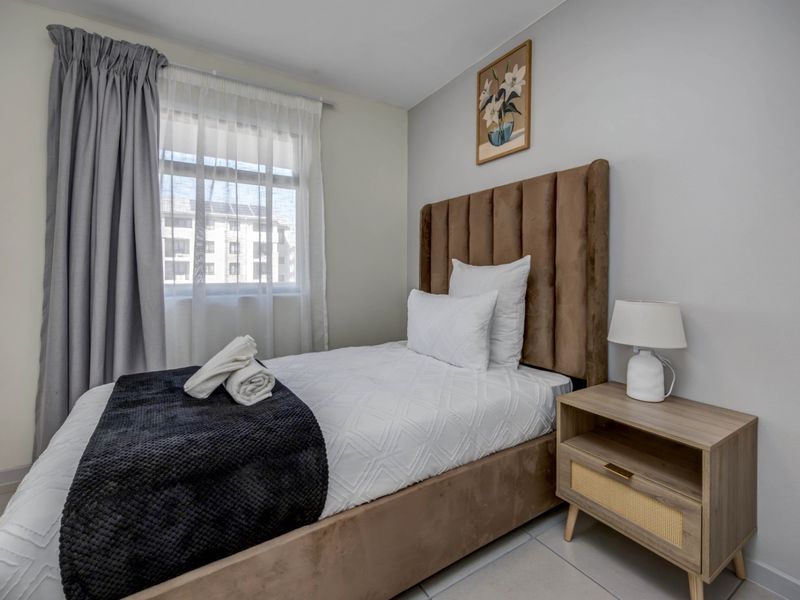 A well-maintained bedroom featuring neutral wall finishes, tiled flooring, and a window with installed curtain tracks.