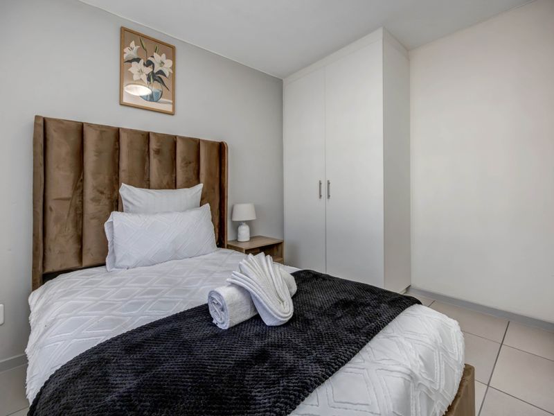 A well-maintained bedroom featuring neutral wall tones, tiled flooring, and a functional built-in wardrobe for storage.