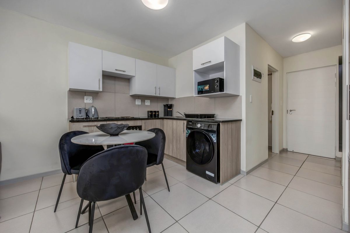 Compact open-plan kitchen featuring modern cabinetry, integrated appliances, and tiled flooring, seamlessly flowing into the living area.