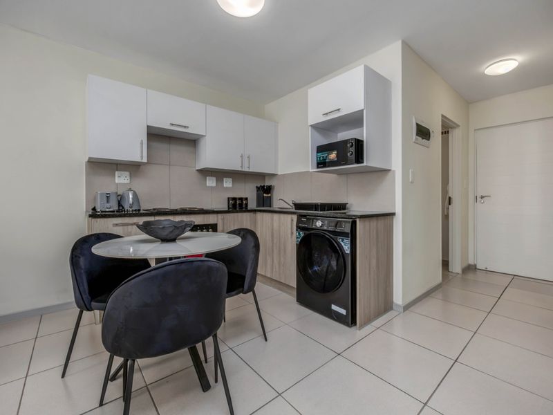 Compact open-plan kitchen featuring modern cabinetry, integrated appliances, and tiled flooring, seamlessly flowing into the living area.