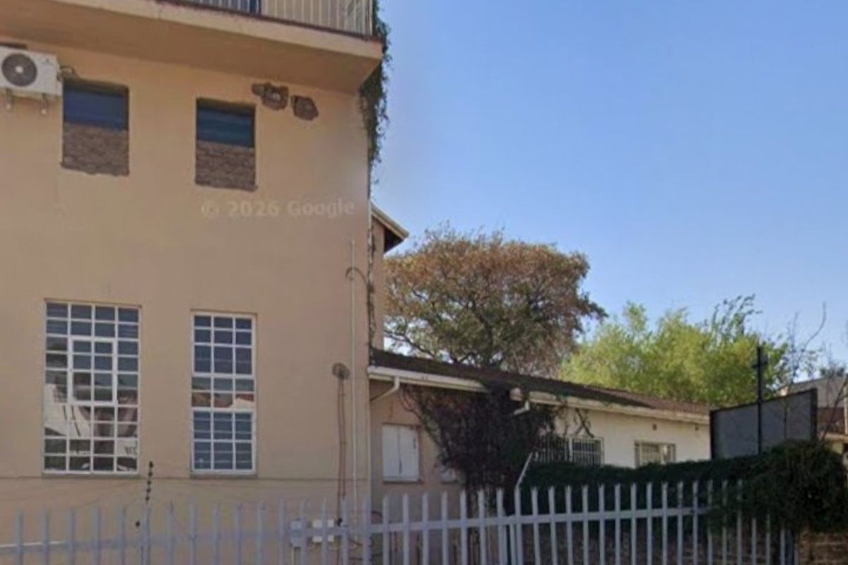 Rear exterior view of a multi-story commercial building featuring a balcony, security fencing, and visible wear to the exterior facade and masonry.