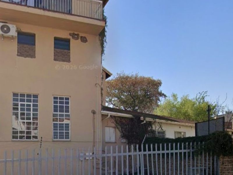 Rear exterior view of a multi-story commercial building featuring a balcony, security fencing, and visible wear to the exterior facade and masonry.