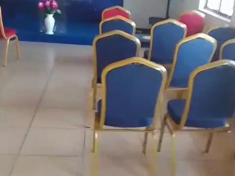 A multi-purpose commercial space featuring tiled flooring, a raised stage area with branding, and a wall-mounted television, suitable for meetings or events.