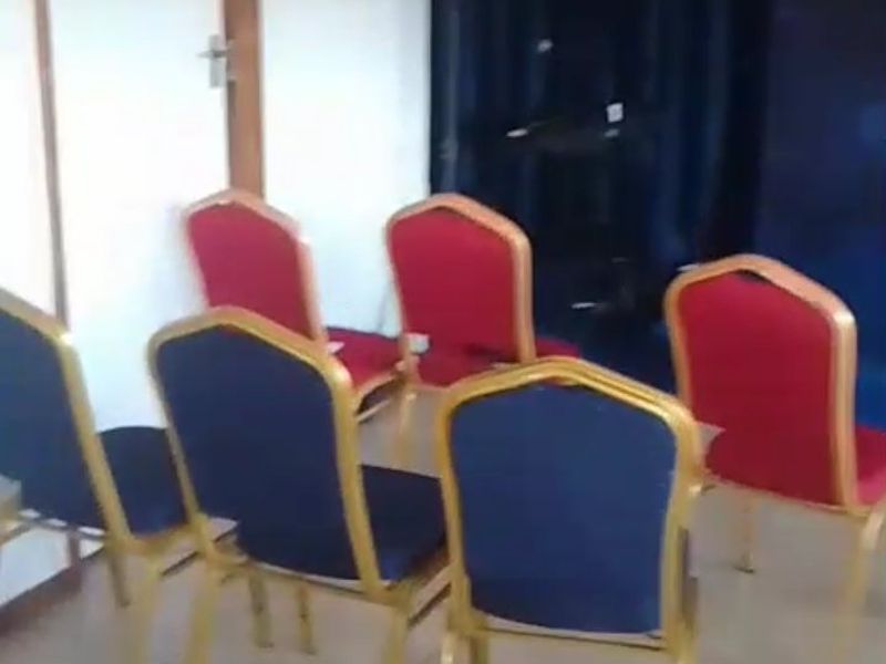 A functional commercial space featuring tiled flooring and a wall-mounted speaker, currently set up with multiple chairs.