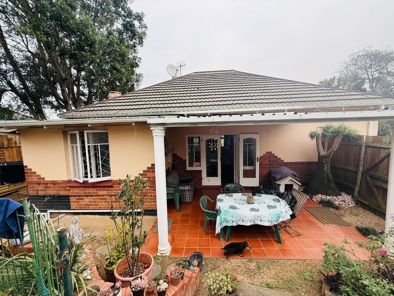 A covered rear patio featuring tiled flooring and decorative columns, providing direct access to the home through double doors.