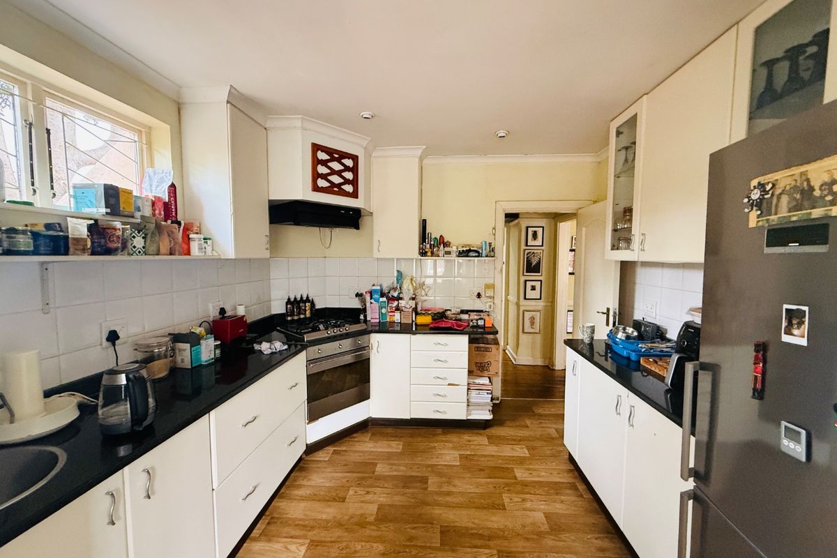 A functional kitchen featuring white cabinetry, dark granite countertops, a gas hob with extractor, and durable laminate flooring.