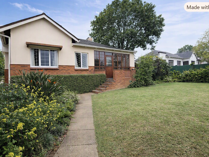 A well-maintained single-story house featuring a brick and plaster facade, a paved walkway, and a spacious front garden.