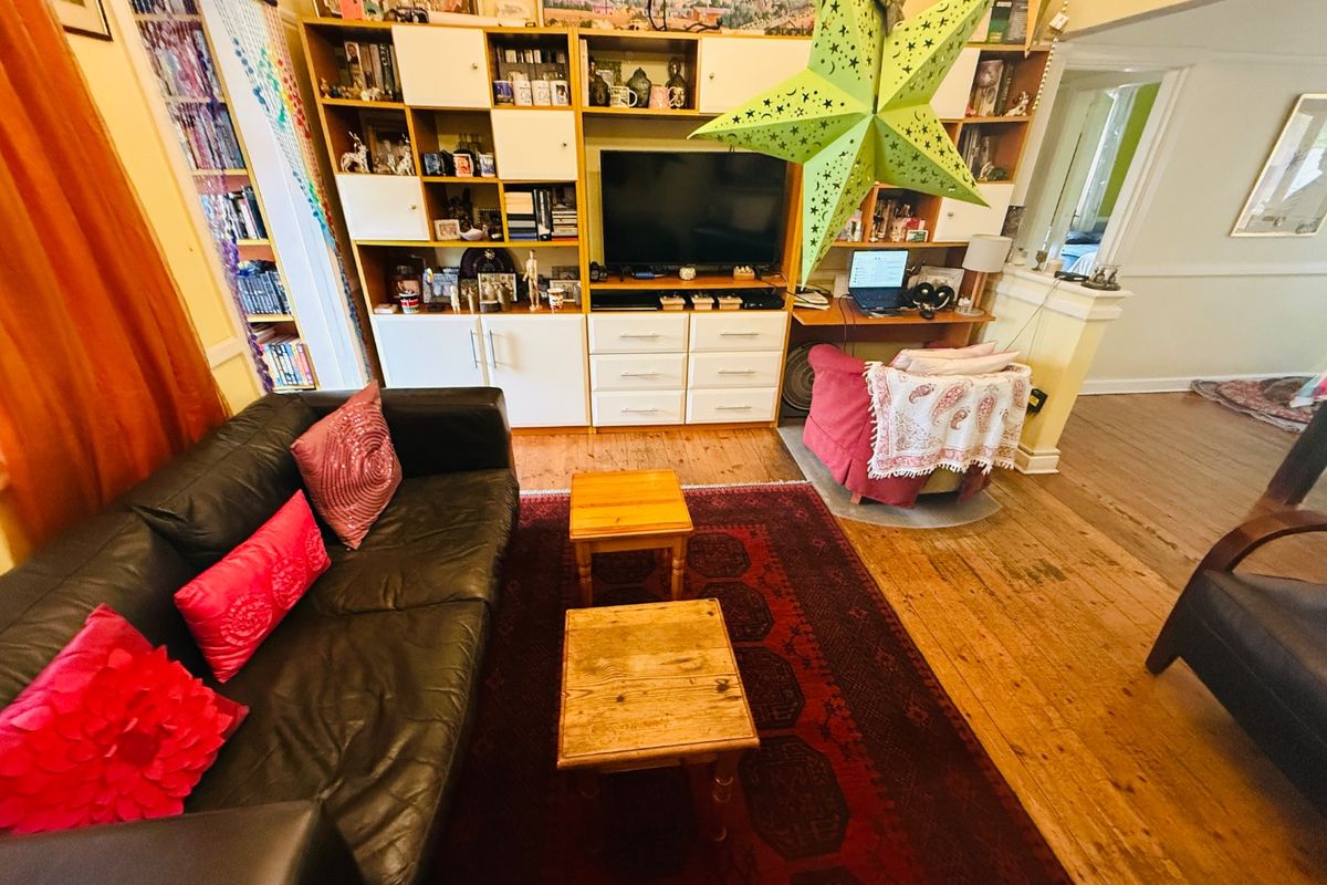 A living room featuring a large built-in shelving unit and original hardwood flooring, offering a functional space with potential for modernization.