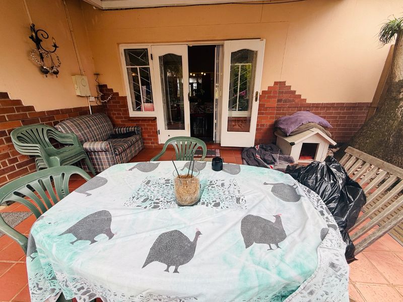 A covered patio area featuring terracotta tiling and brick accents, providing direct access to the interior through double glass doors.
