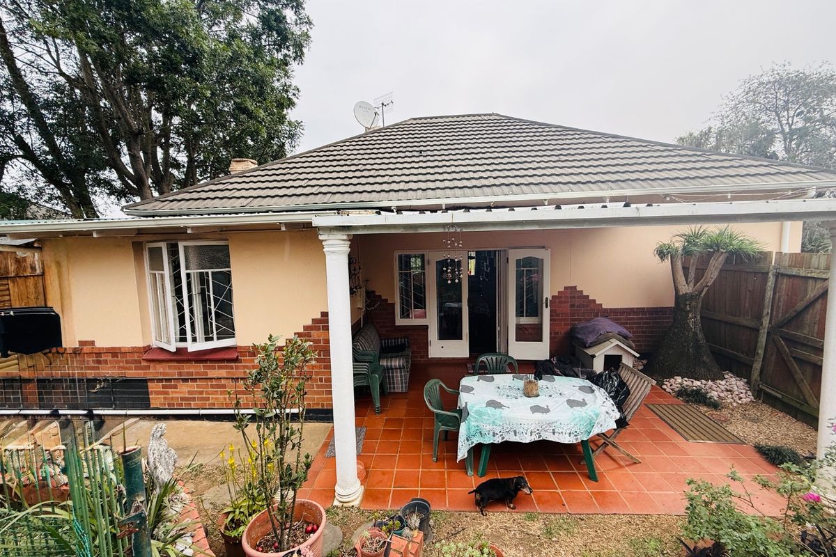 Rear view of the house featuring a covered tiled patio, brick and plaster facade, and classic french doors leading into the home.