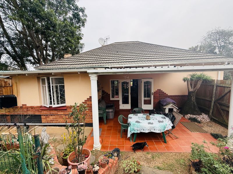 Rear view of the house featuring a covered tiled patio, brick and plaster facade, and classic french doors leading into the home.