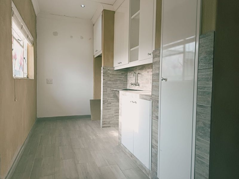 A functional scullery area featuring built-in white cabinetry, tiled backsplash, and tiled flooring, providing a clean and organized utility space.