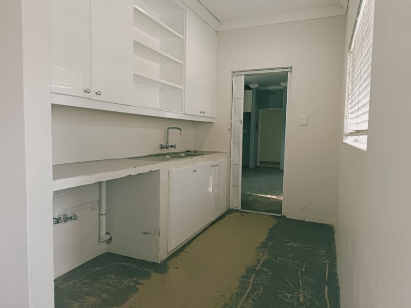 A functional laundry room featuring built-in cabinetry, a stainless steel sink, and plumbing connections, currently awaiting final flooring installation.