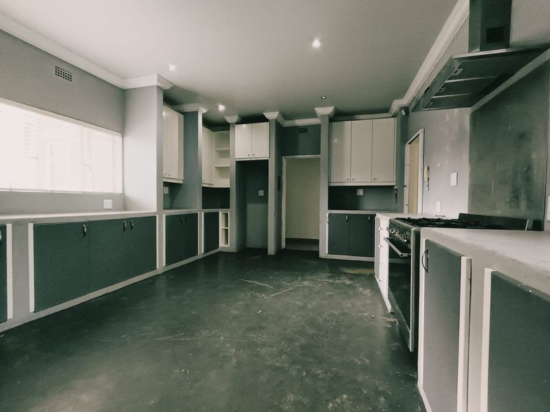 An empty kitchen featuring built-in cabinetry, a freestanding stove with an extractor fan, and recessed lighting, offering a blank canvas for renovation.