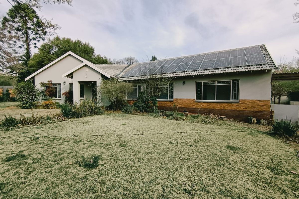 Rear view of a single-story house featuring a large lawn, brick and plaster exterior, and a roof equipped with solar panels.