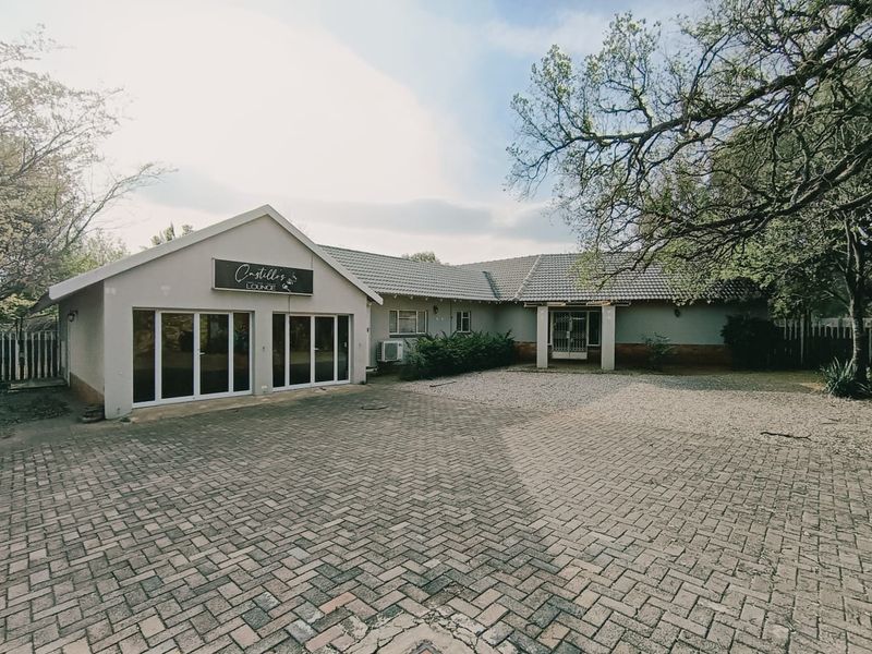 Front exterior view of the property featuring a large paved driveway, tiled roof, and sliding glass entrance doors.