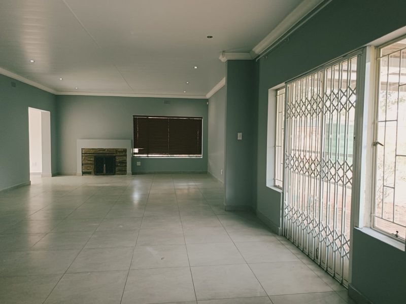Spacious, light-filled living area featuring neutral tiled flooring, a stone-clad fireplace, and secure sliding door access to the exterior.
