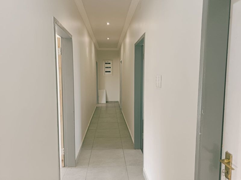 A clean, well-lit hallway featuring neutral wall finishes, tiled flooring, and multiple doorways leading to adjacent rooms.