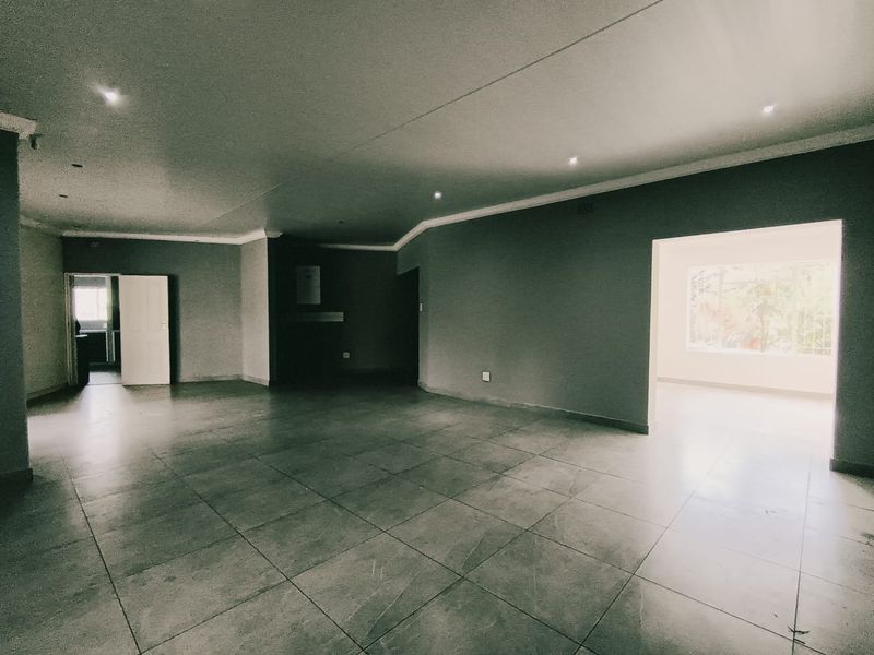 Spacious open-plan living area featuring large format floor tiles, recessed downlighting, and neutral wall finishes, offering a versatile layout for modern living.
